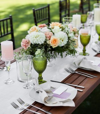 dinner tables with white tablecloth, served with porcelain and green glasses. Georgeous wedding table decorated with flowers