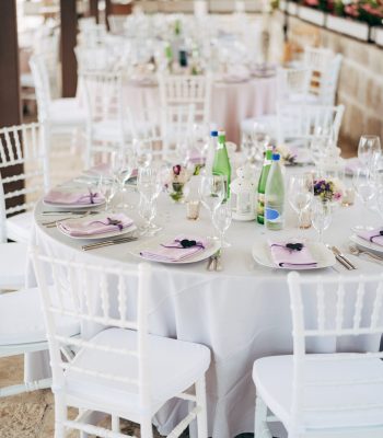Round banquet table with white tablecloth and white Chiavari chairs. Wedding under the tent.